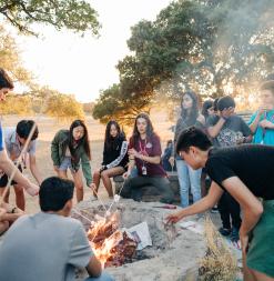 Participants enjoy a bonfire together, roasting marshmallows. 