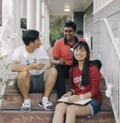 Three participants sit on different steps on the stoop of the SUMaC dorm.